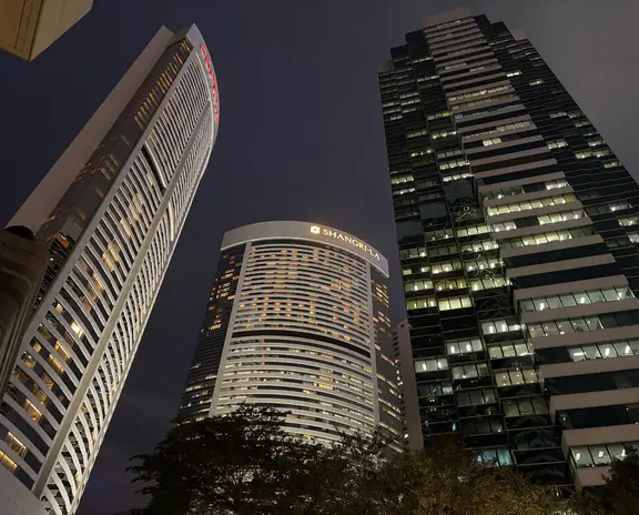 Nighttime cityscape with tall illuminated skyscrapers and a curved white building in the foreground.