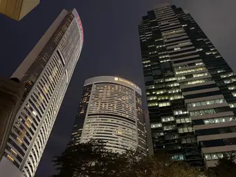 Nighttime cityscape with tall illuminated skyscrapers and a curved white building in the foreground.