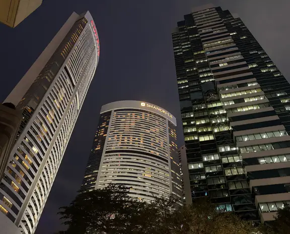 Nighttime cityscape with tall illuminated skyscrapers and a curved white building in the foreground.
