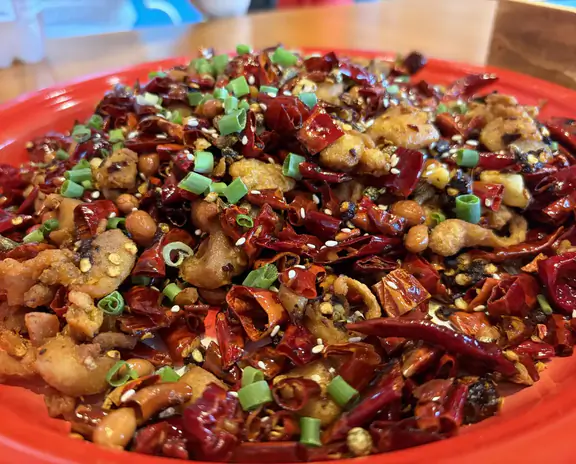 A colorful plate of stir-fried dish with red chilies, chopped green onions, and fried morsels on a red plate.