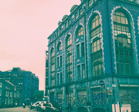 Street view of a large historic building with arched windows on a corner, storefronts at street level.